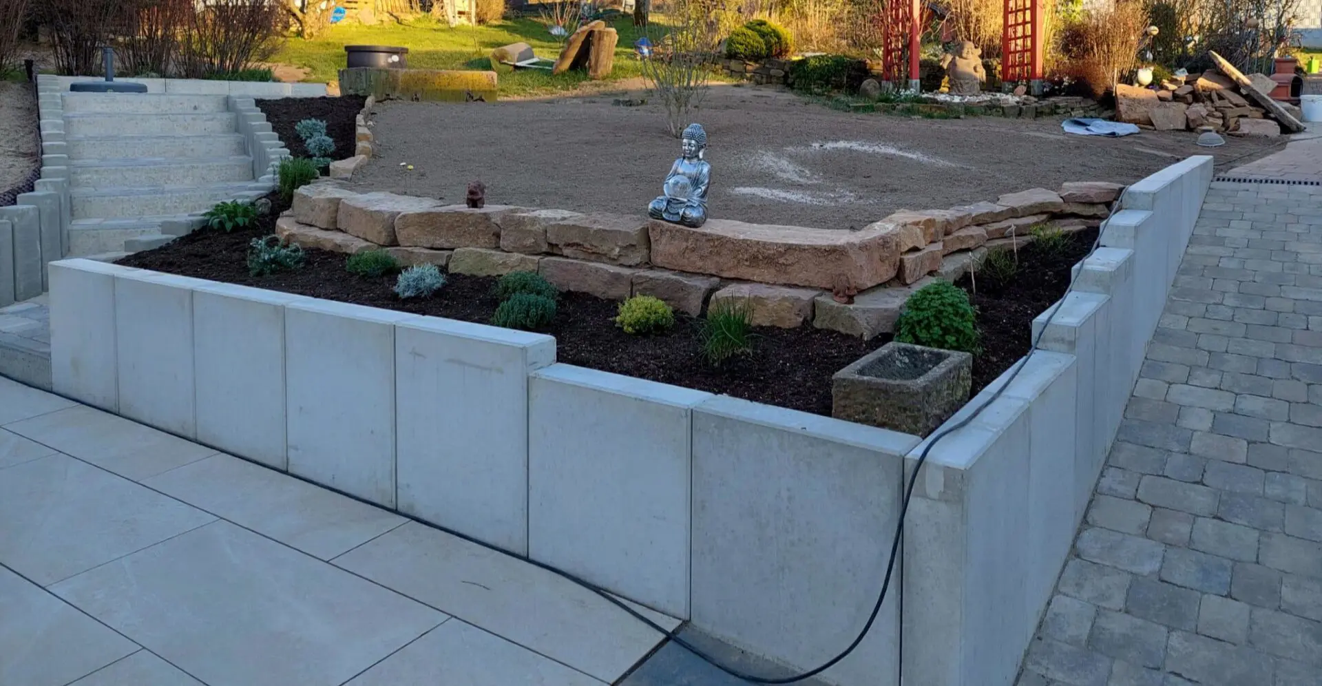 Hangsicherung und Beeteinfassung durch Mauerscheiben und Natursteintrockenmauer aus rotem Sandstein, Treppenanlage eingefasst mit Betonpalisaden und gepflasterter Rampe mit Heidelberger Kopfsteinpflaster im Reihenverband