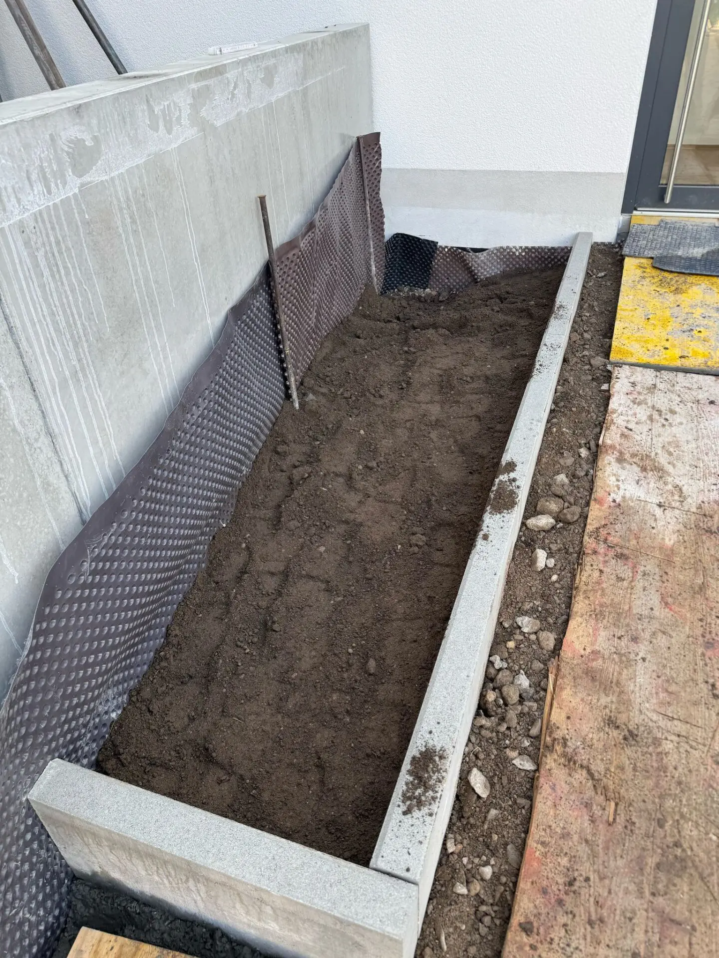 Beeteinfassung aus Tiefbord an Hauszugang und Sichtbetonmauerwerk