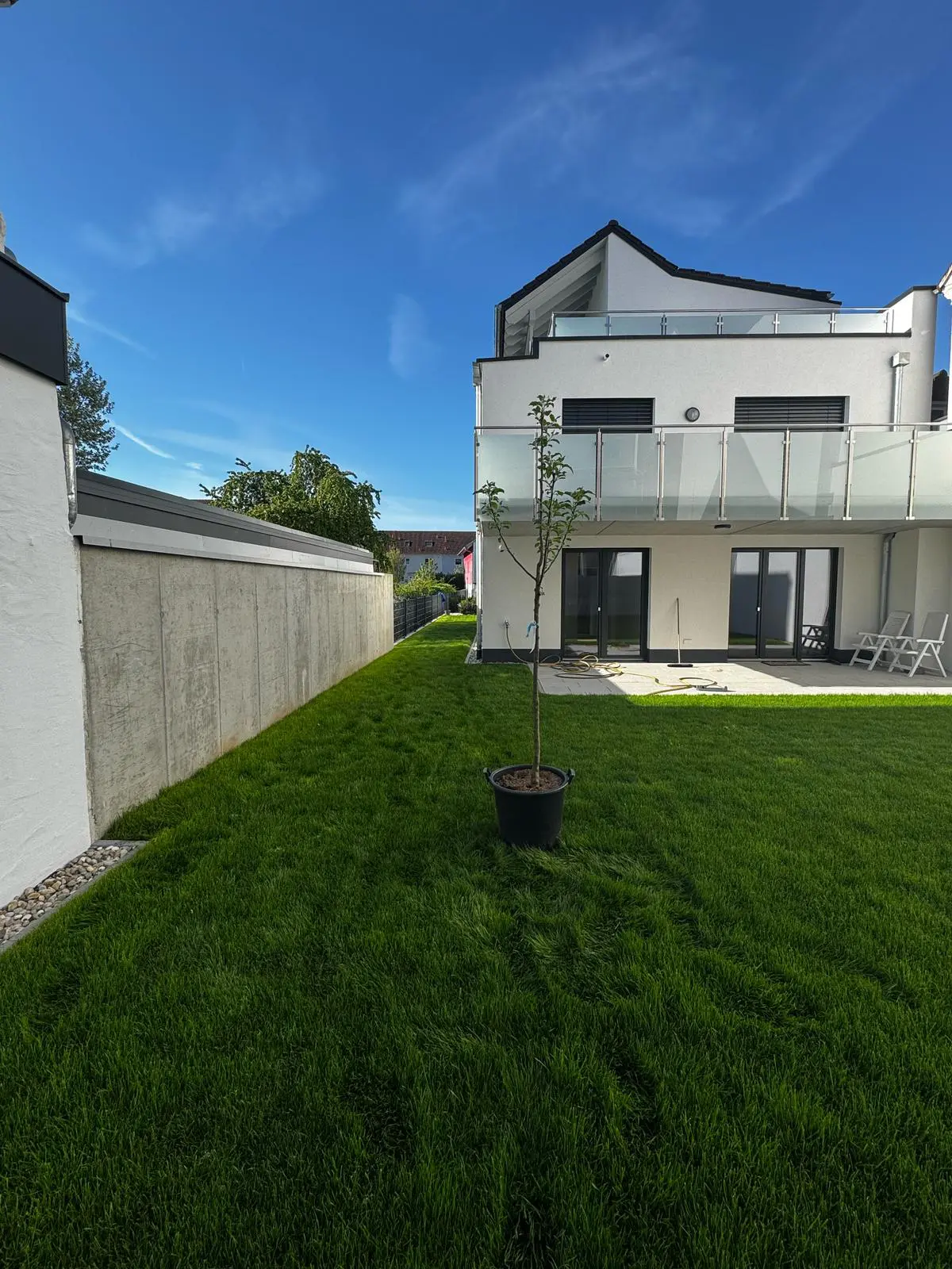 Terrasse mit Feinsteinzeugplatte 60x60x2cm in beige (hier in Splitt verlegt optional auch in 1-Korn Beton) umgeben von grünem Rollrasen (Classic Sport)