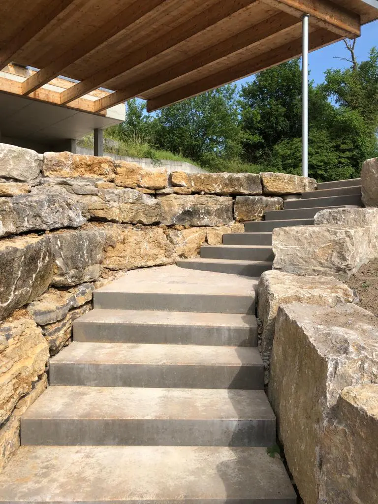 Hangsicherung durch Anlegen von Terrassen mit Naturstein Jura-Kalk Böschungssteinen C1 (50-60cm hoch und tief) mit Treppenanlage aus Blockstufen integriert