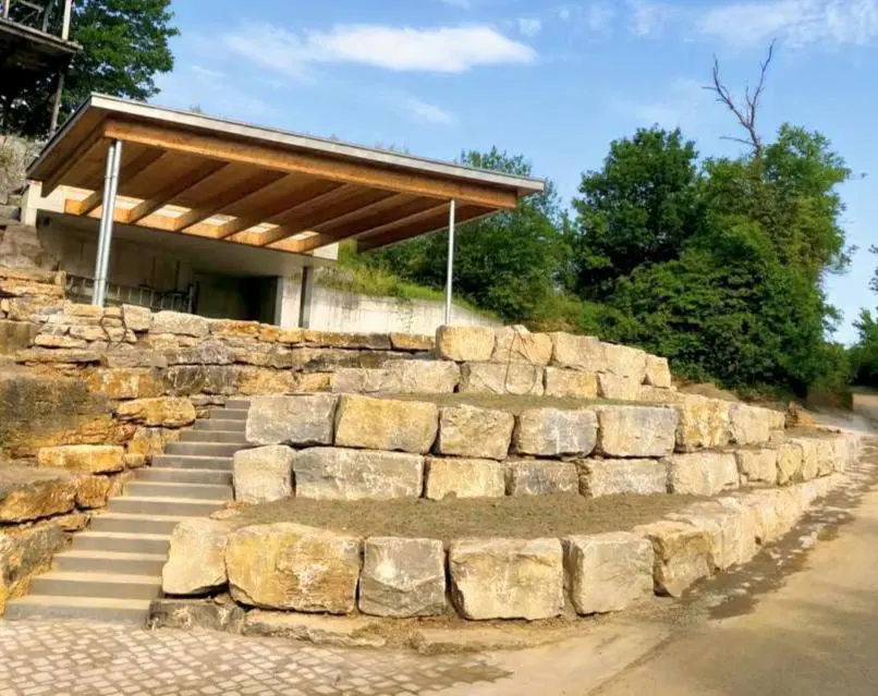 Hangsicherung durch Anlegen von Terrassen mit Naturstein Jura-Kalk Böschungssteinen C1 (50-60cm hoch und tief) mit Treppenanlage aus Blockstufen integriert