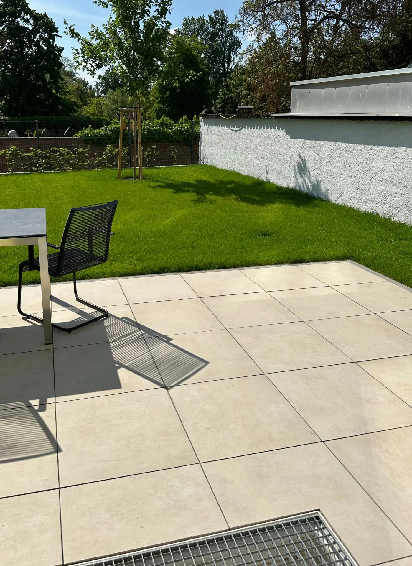 Terrasse mit Feinsteinzeugplatte 60x60x2cm in beige (hier in Splitt verlegt optional auch in 1-Korn Beton), mit Garten begrünt mit Rollrasen (Classic-Sport), Baum (Feldahorn) und Hainbuchenhecke vor Doppelstabmattenzaun