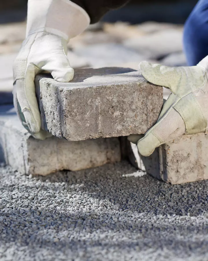 Nahaufnahme der Hände eines Arbeiters, der einen Pflasterstein auf einem Weg verlegt