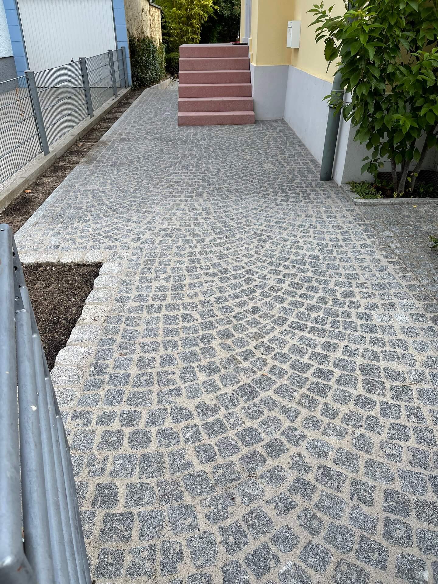 Natursteinkleinpflaster Granit im Segmentbogen verlegt, mit Pflasterfugenmörtel verfugt sowie Treppenanlage aus eingefärbten Blockstufen für Hauszugang