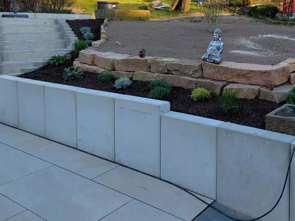 Terrassengarten mit Stufen, einer niedrigen Steinmauer und einer kleinen Buddha-Statue auf der Mauer